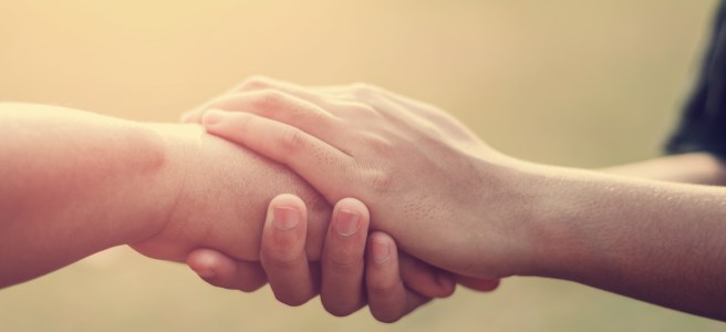 two hands reaching together in support for sarcastic article on the pain the press has caused Archbishop Chaput