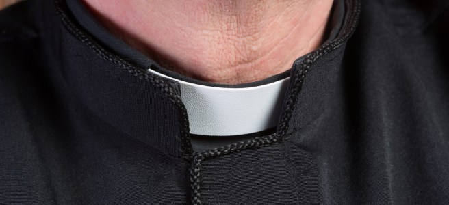 Closeup of the neck of a priest wearing a black shirt with cassock and white clerical collar